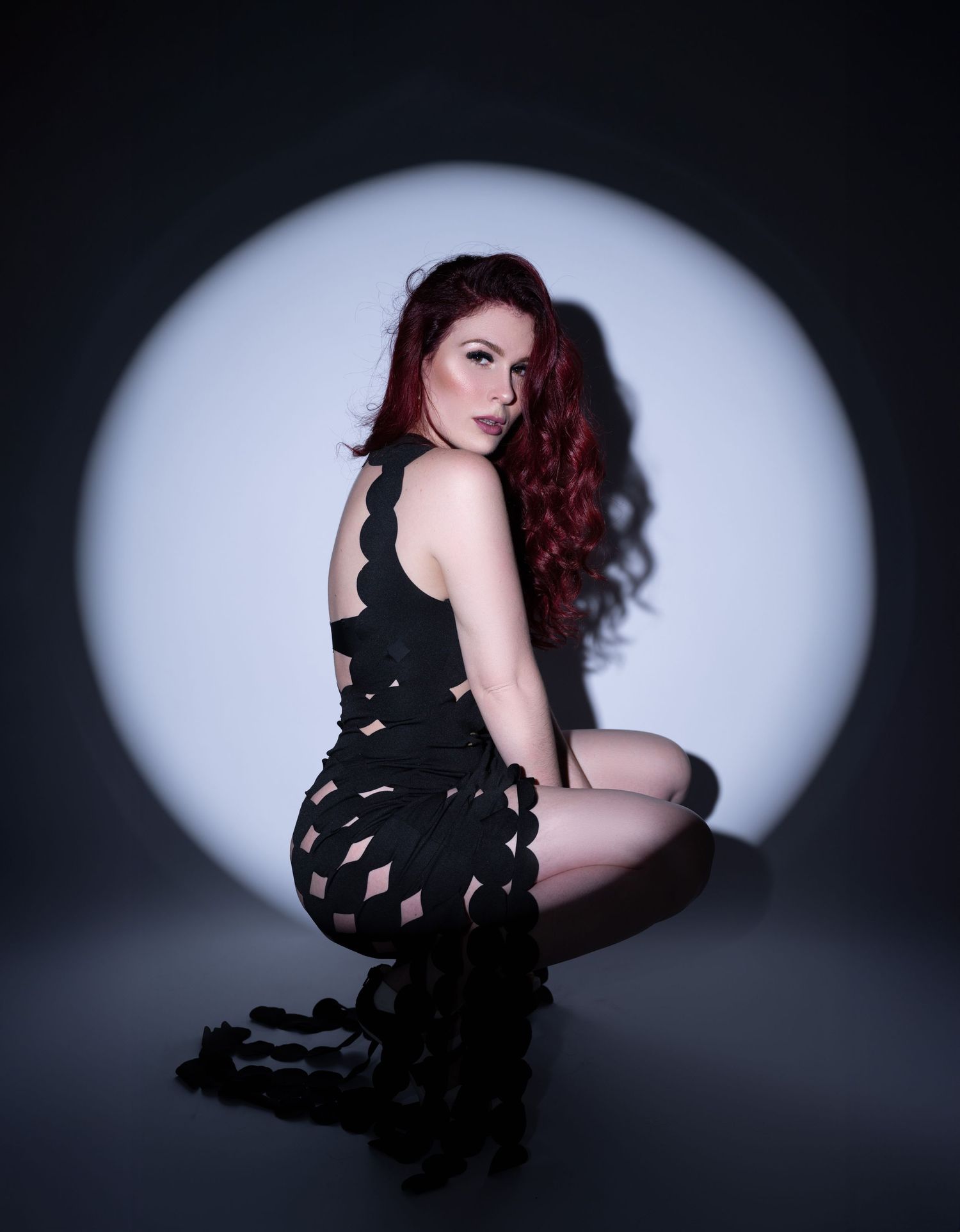 Artistic portrait with silhouette against white circular backdrop wearing black patterned dress.
