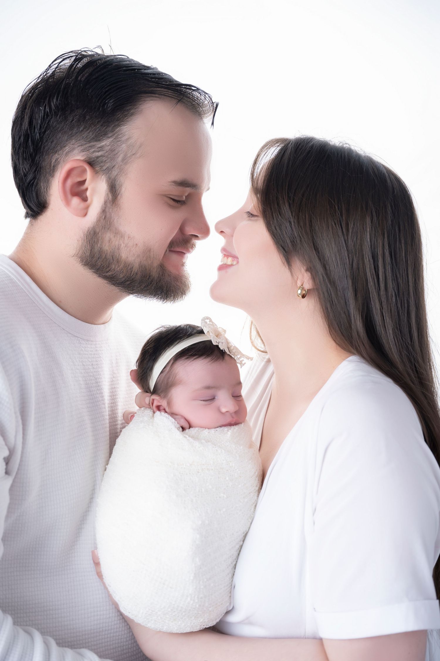 Intimate family portrait with newborn swaddled in white against light background.