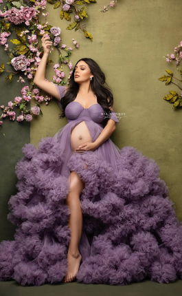 A figure in a flowing purple tulle gown poses gracefully against a sage green backdrop with cherry blossoms.