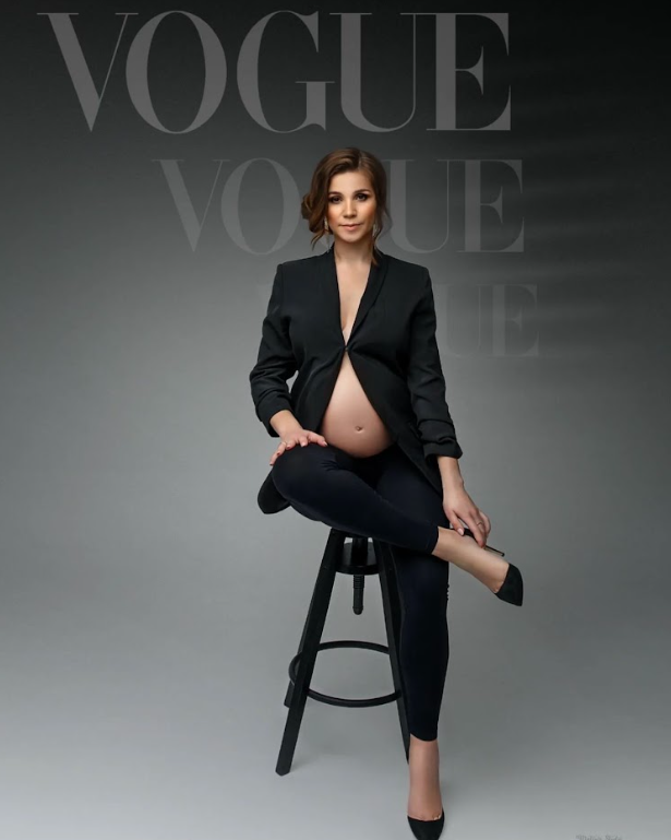 Maternity fashion photo for Vogue magazine featuring elegant black suit and heels against gray backdrop.