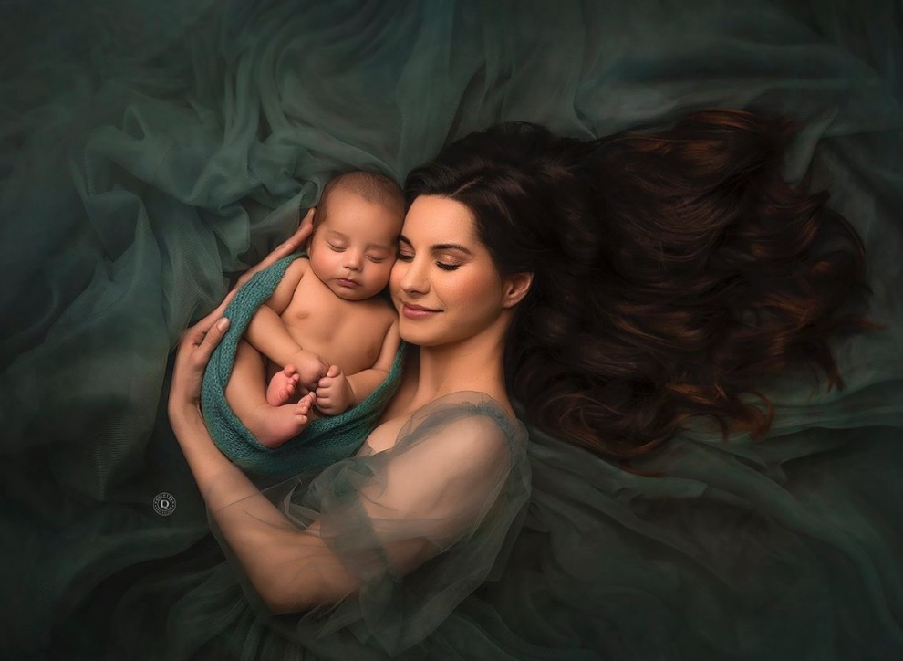 A tender artistic portrait series showing a parent and baby in dark moody lighting with flowing fabric and ethereal atmosphere.
