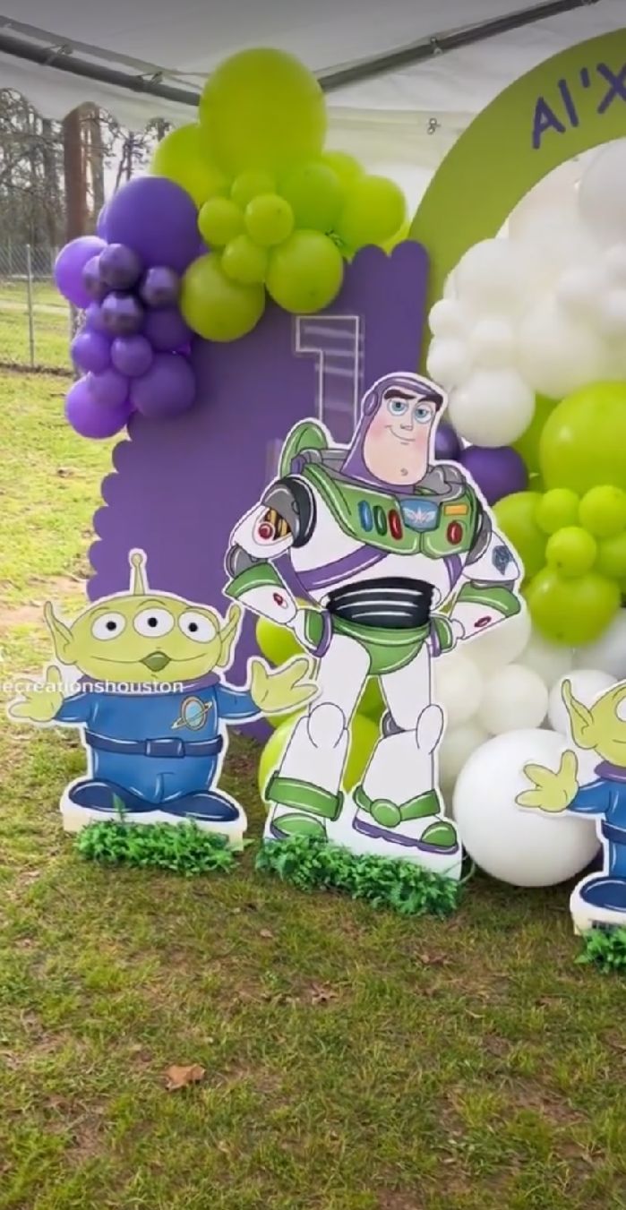 Toy Story themed party decorations with Buzz Lightyear cutouts and purple and green balloon garland on grass.