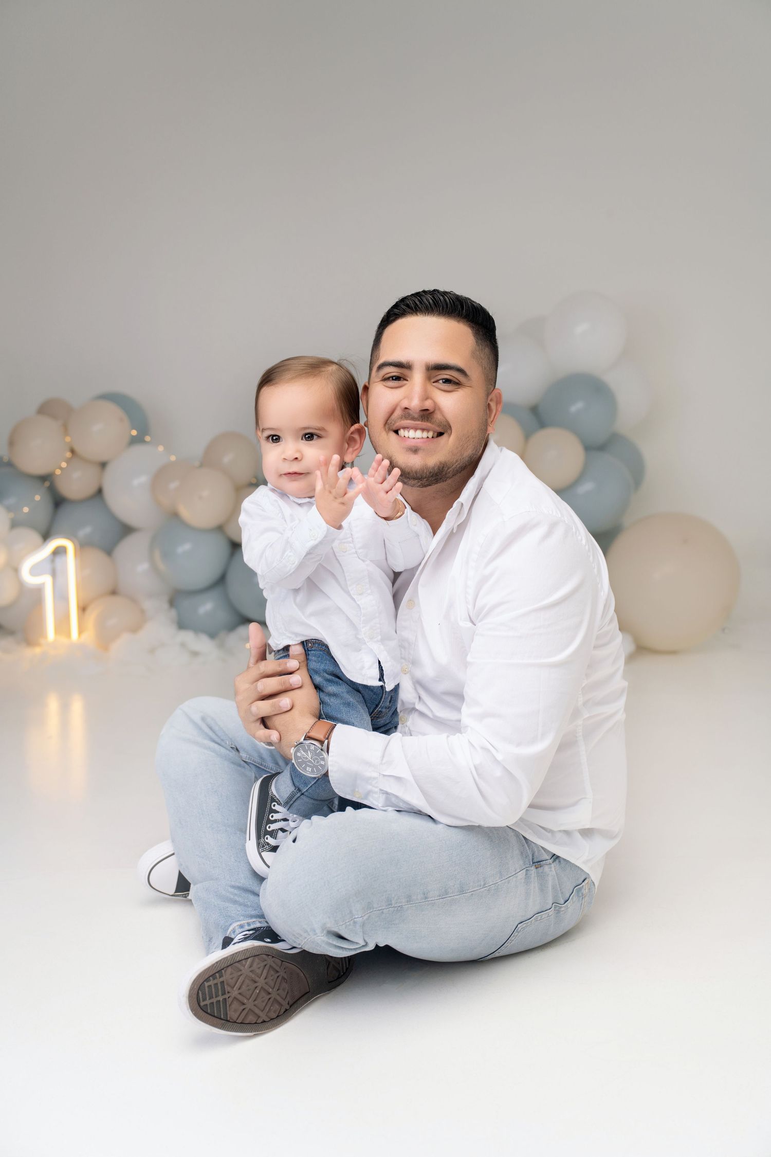 Father holding baby at first birthday photoshoot with balloons and number one decoration.