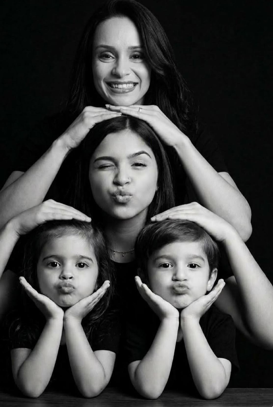 Black and white family portrait of a woman and three children posing playfully with duck faces and hands on cheeks.