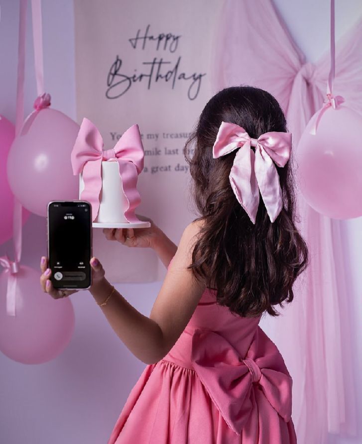 Pink birthday celebration setup with balloons and bows showing someone taking photos.