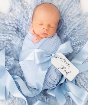 A sleeping newborn baby wrapped in soft blue swaddle blankets on a textured gray backdrop.