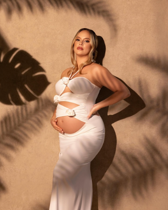 Artistic maternity photography with dramatic palm leaf shadows cast on a warm beige background.