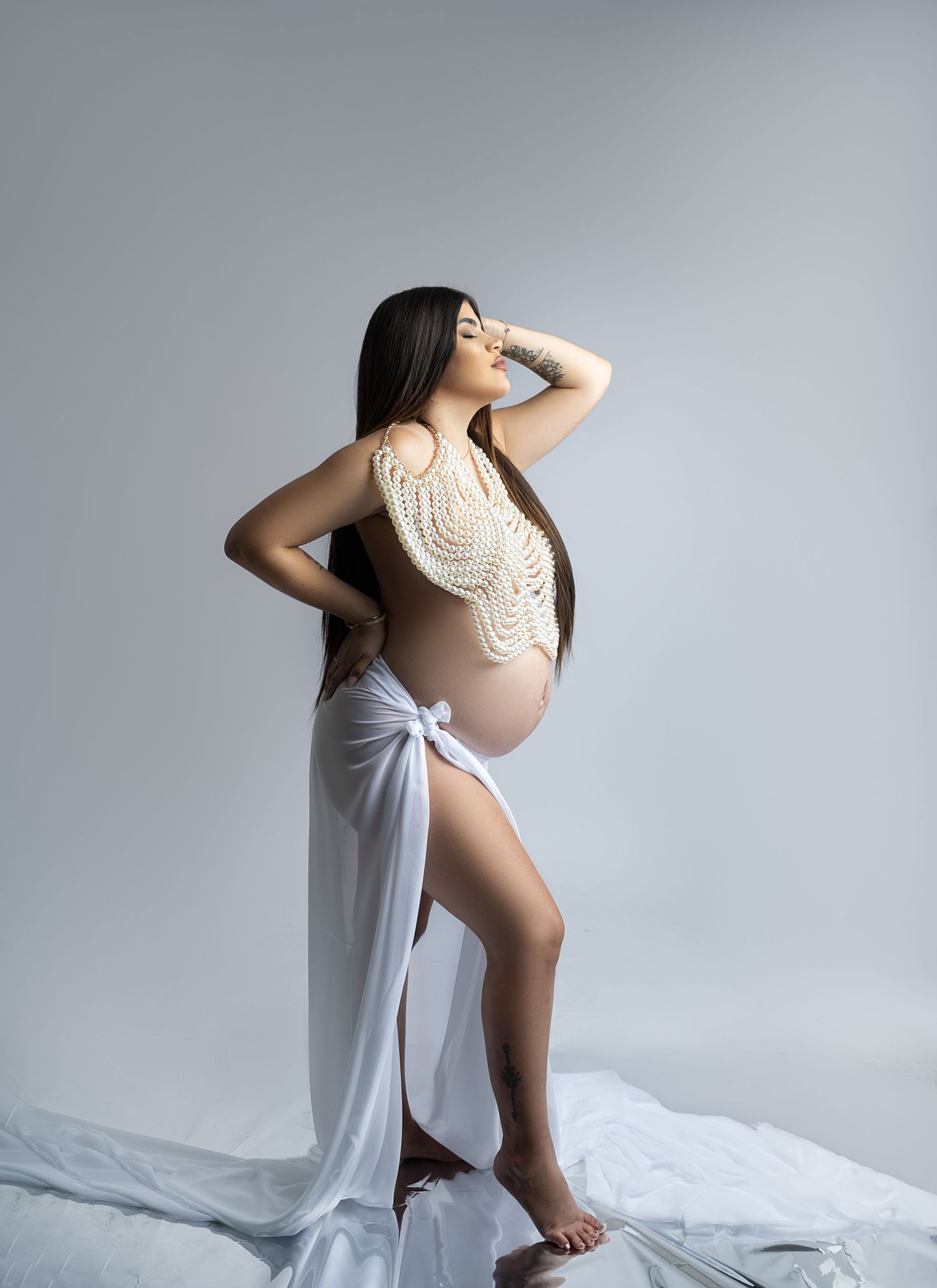 Artistic maternity portrait in white lace bodysuit with flowing fabric.