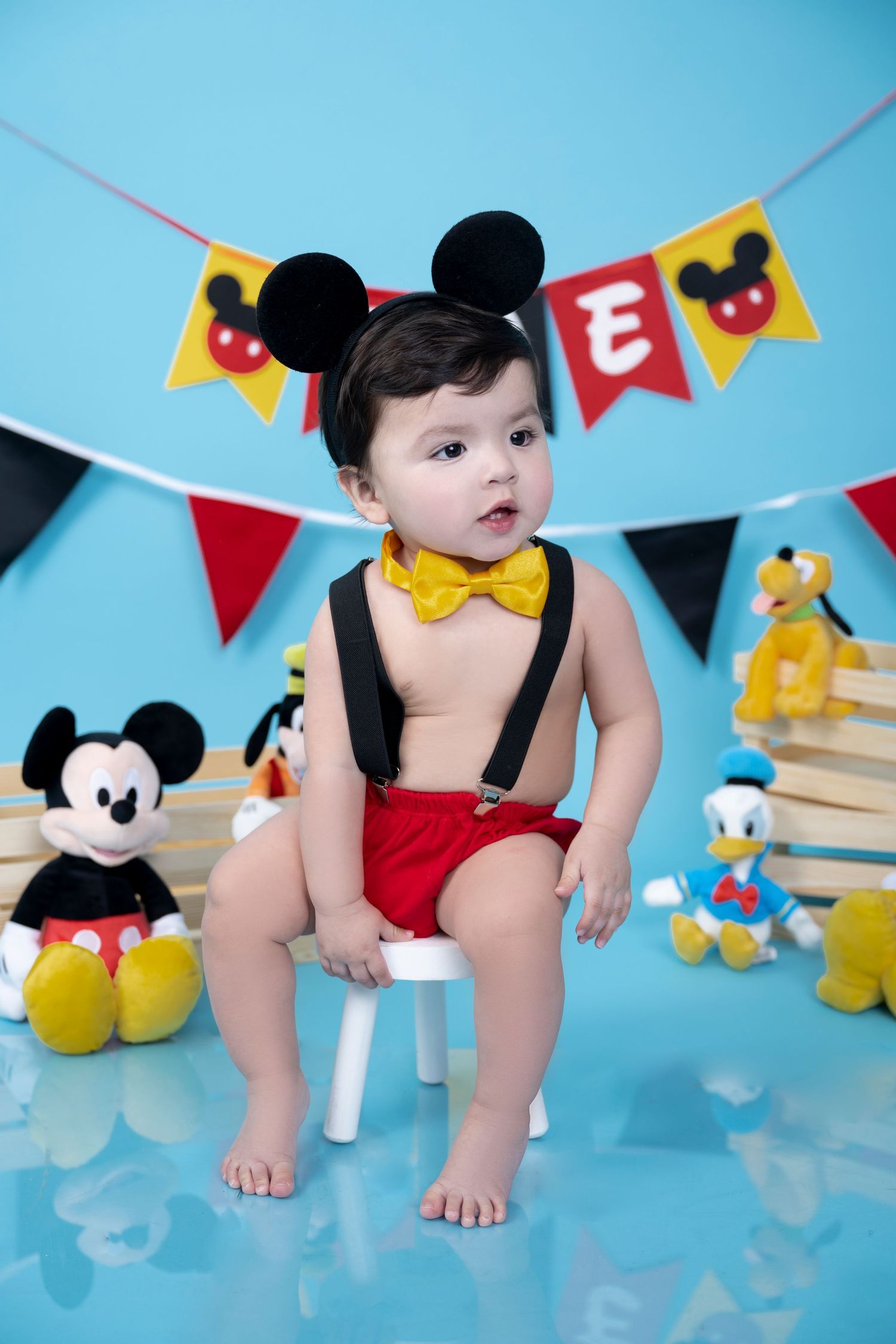 Mickey Mouse themed photo shoot with toys and festive banners on blue backdrop.