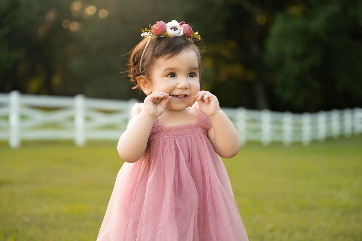 A joyful portrait in a pink dress with a white fence backdrop.