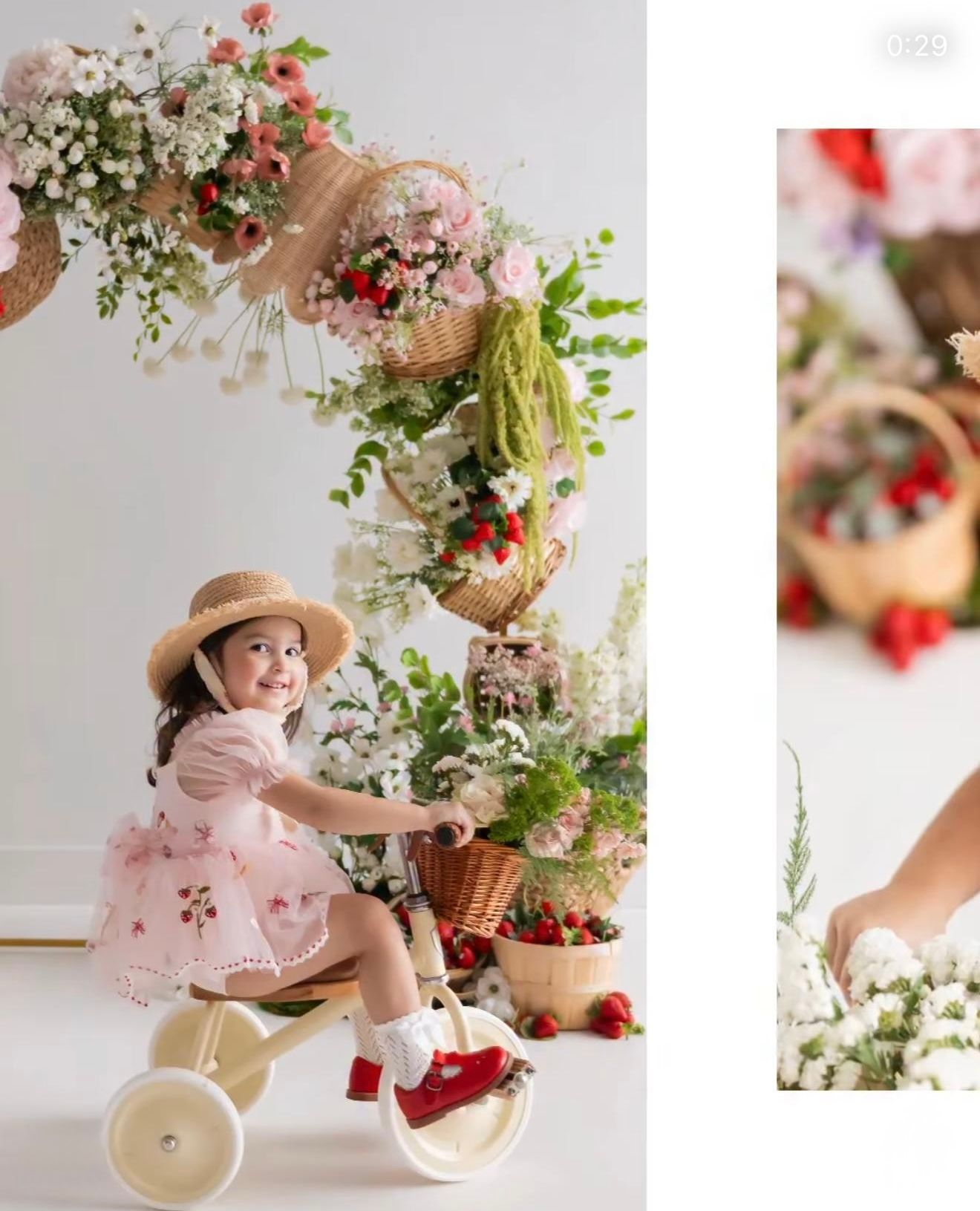 A toddler girl in a pink dress and straw hat rides a tricycle surrounded by floral arrangements and wicker baskets.