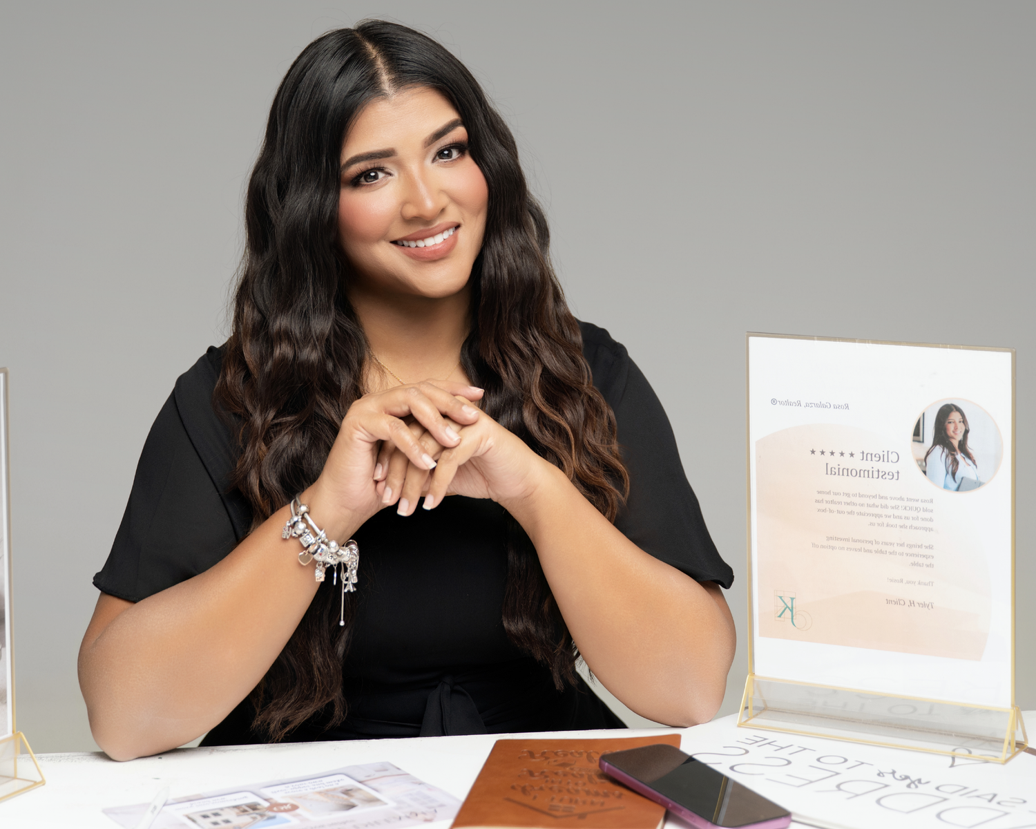 Professional woman in black top sits at desk smiling, with branded display sign and accessories nearby.