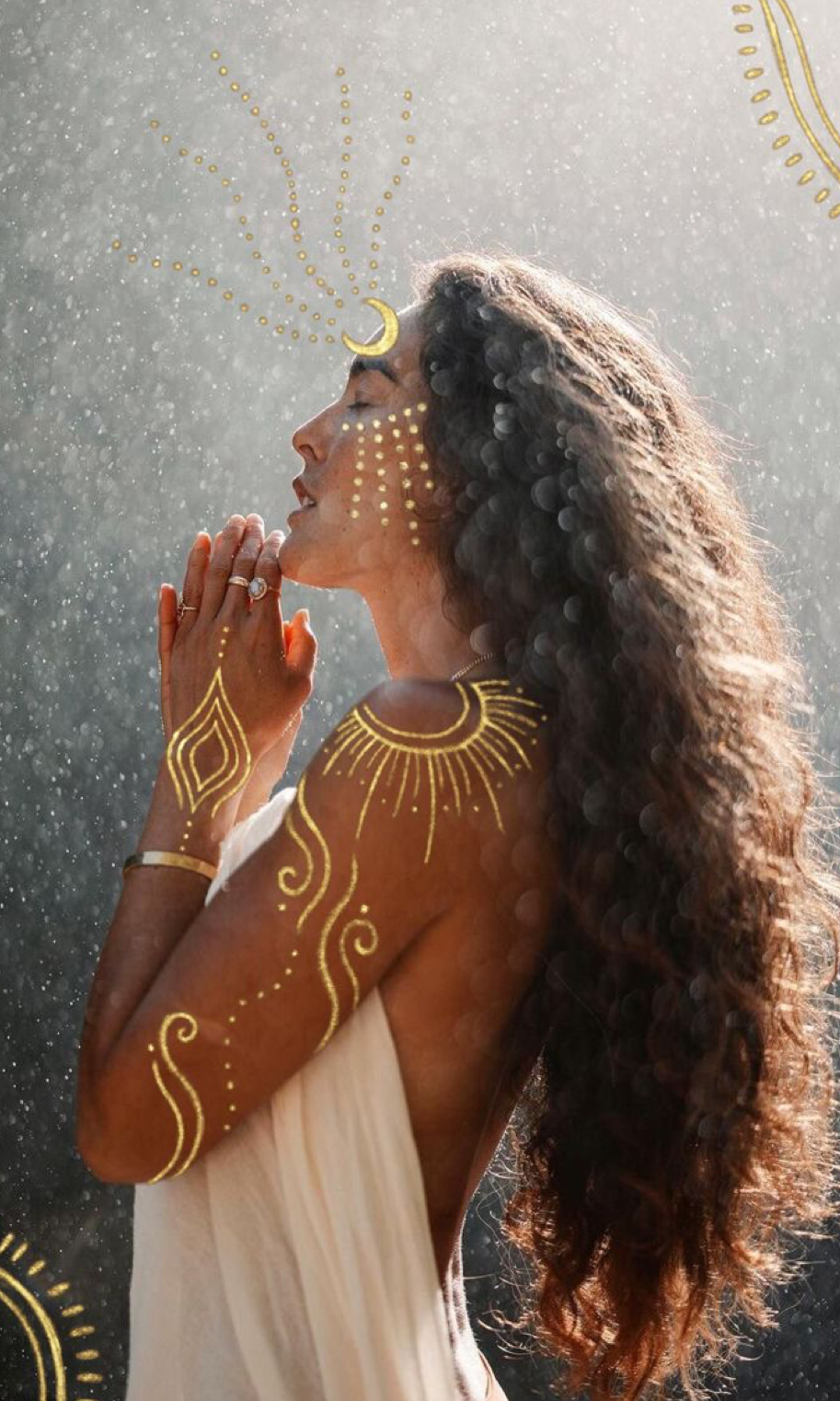 Woman with golden henna body art and crescent moon forehead, hands in prayer pose, long curly hair, spiritual aesthetic.