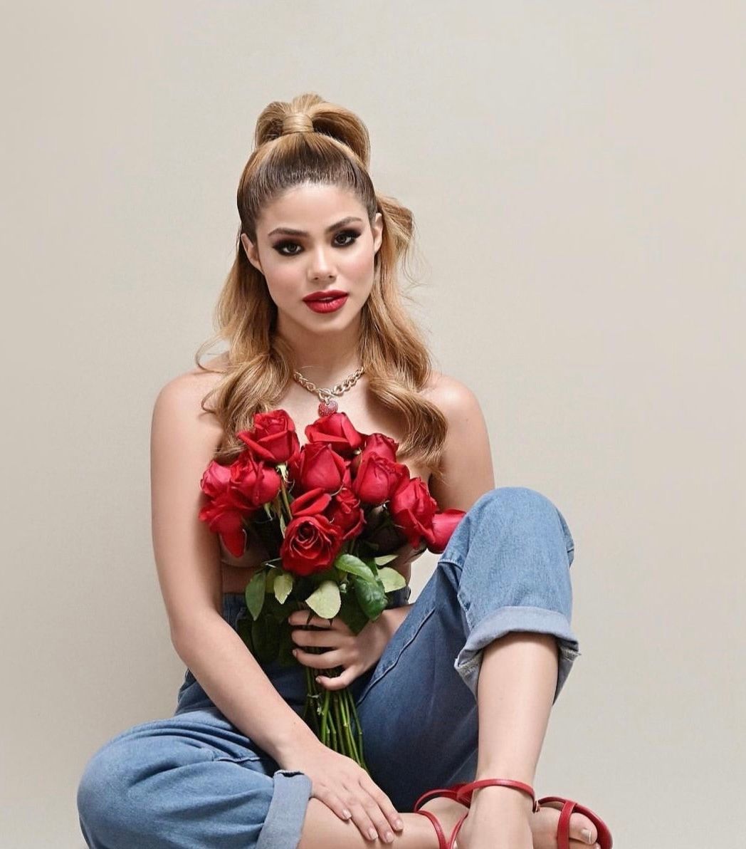 Woman with blonde hair holding red roses bouquet, wearing jeans and strapless top with diamond necklace.
