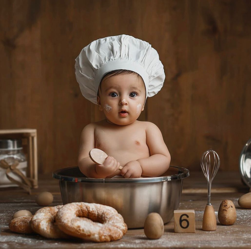 Baking themed baby photo with mixing bowl, whisk, and donuts against wooden backdrop.