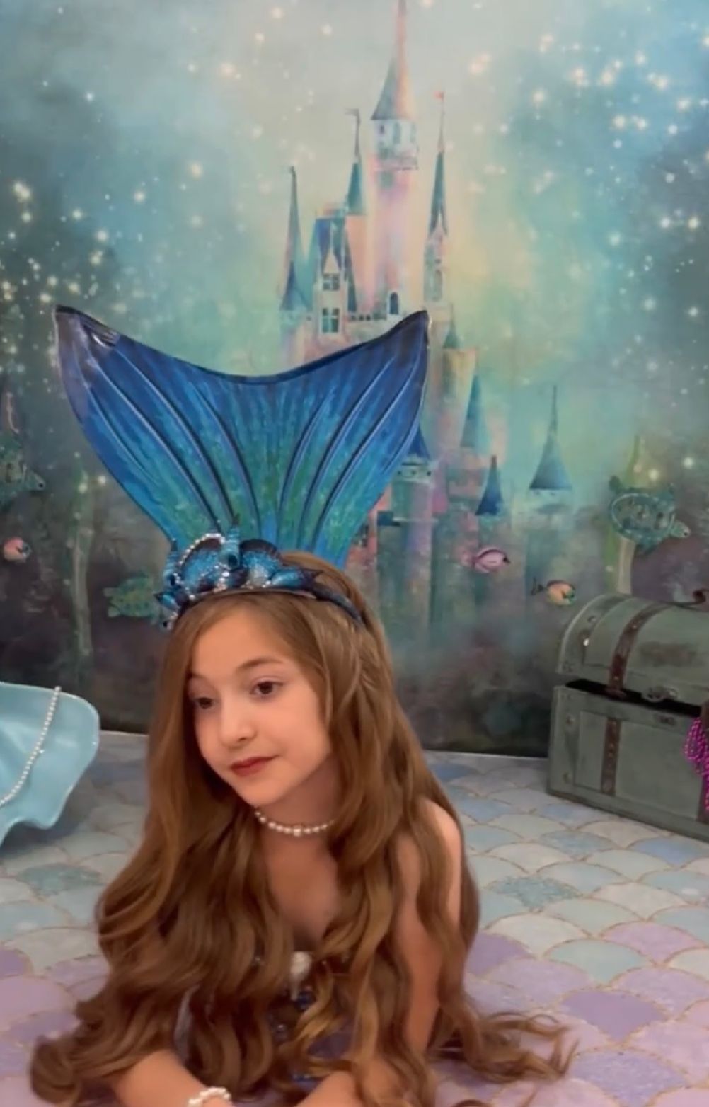 A dreamy underwater-themed photo set with a castle backdrop and mermaid tail props in shimmering blue and teal tones.