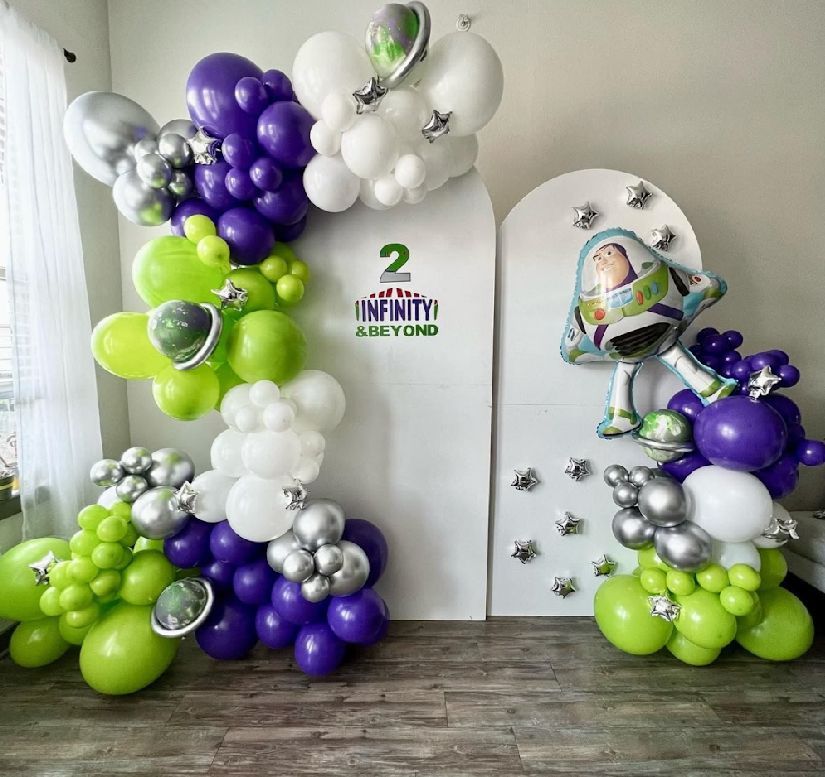 Modern party setup with purple and lime green balloon garland arch against a white wall with space theme decor.