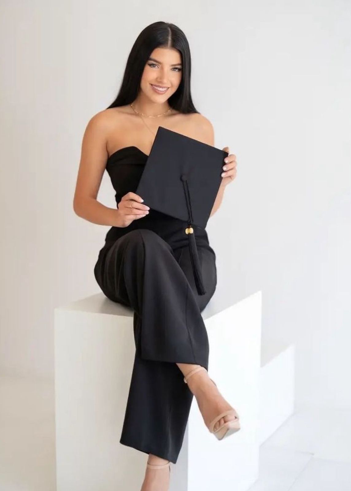 A series of graduation photos showing someone in a black dress and graduation gown posing with their diploma against a white wall.