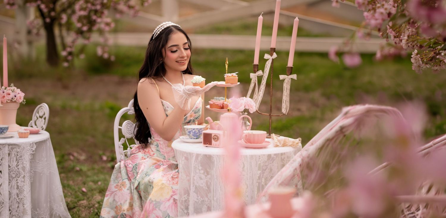 Young woman in floral dress at elegant pink outdoor tea party with cherry blossoms in spring garden.