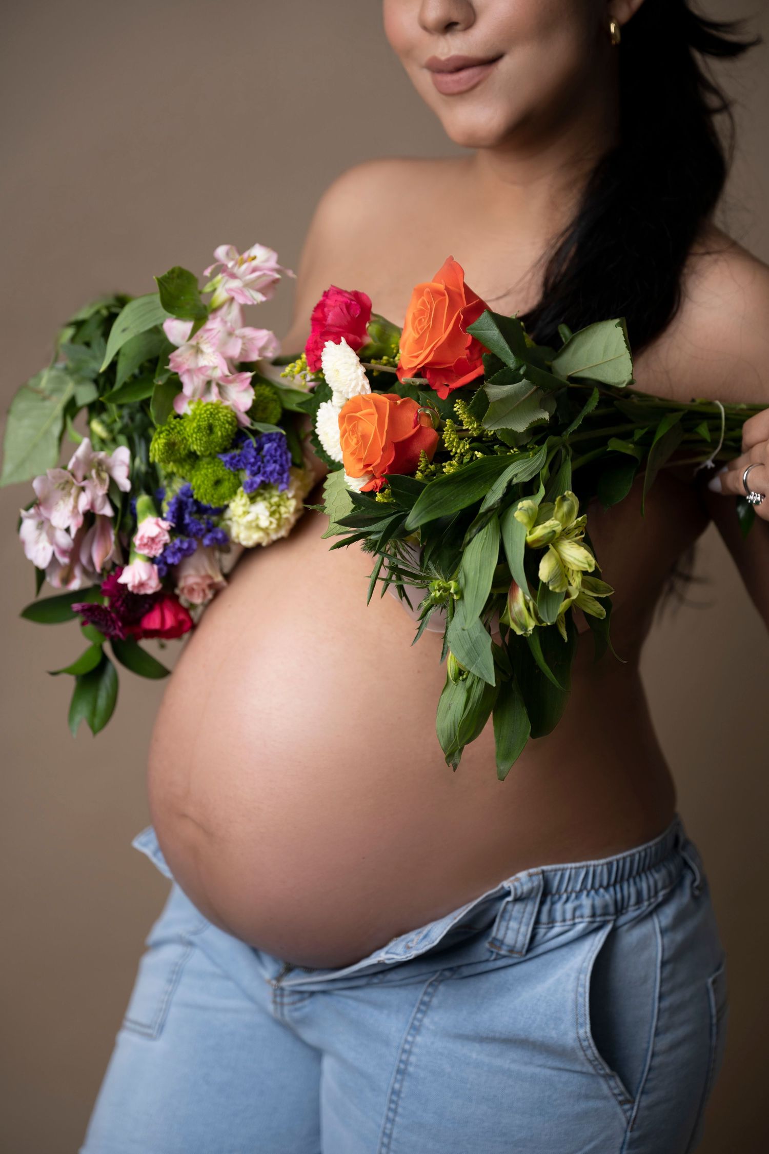 A pregnant woman's belly adorned with colorful flowers including roses, hydrangeas and greenery against a neutral background.
