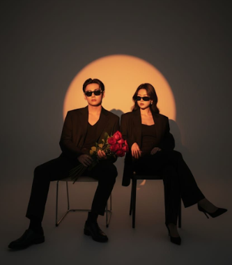 Two figures in dark clothing sit against a sunset-like orange backdrop in a dramatic silhouette series.