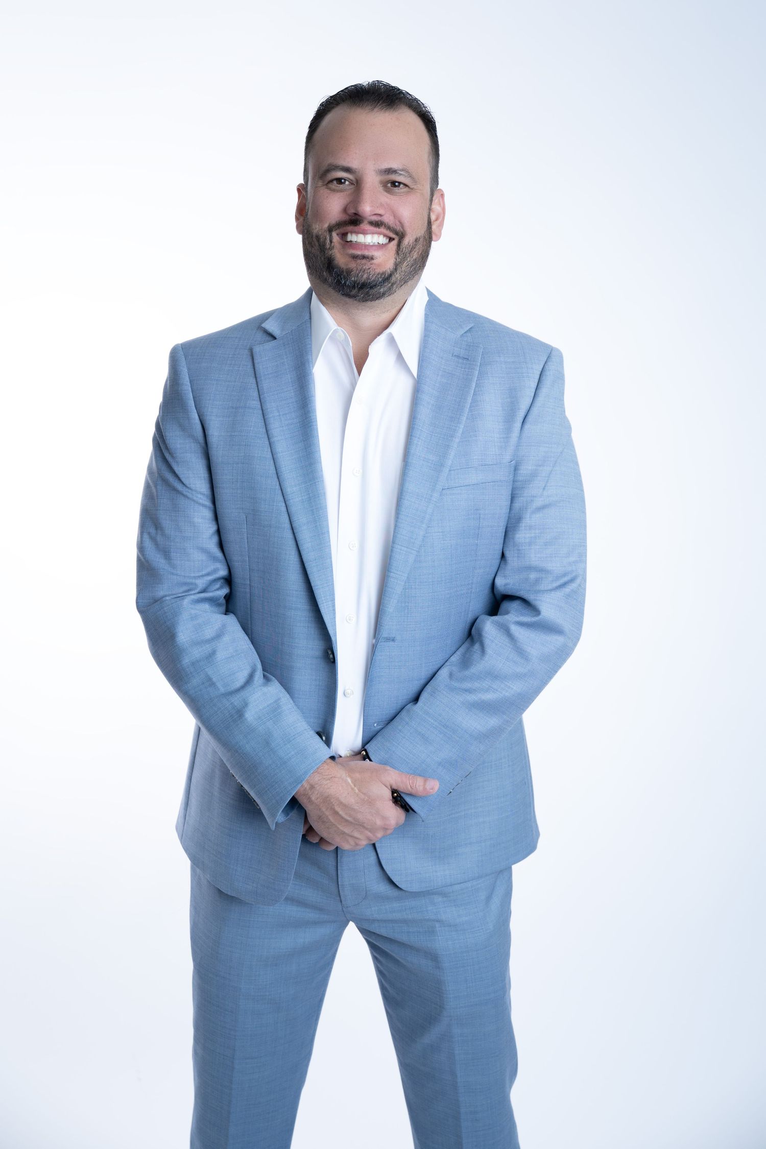 Professional wearing a light blue suit and white dress shirt poses confidently against white background.