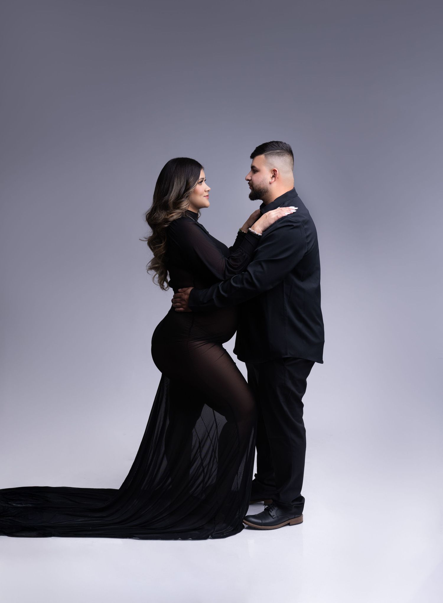 Studio portrait of couple in black attire sharing intimate moment against grey background.