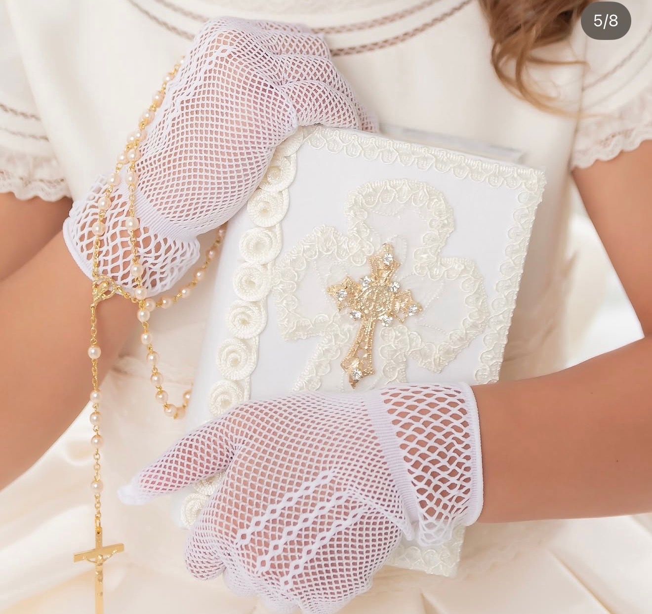 Girl holding white Bible and rosary wearing white lace fishnet gloves for First Holy Communion ceremony.