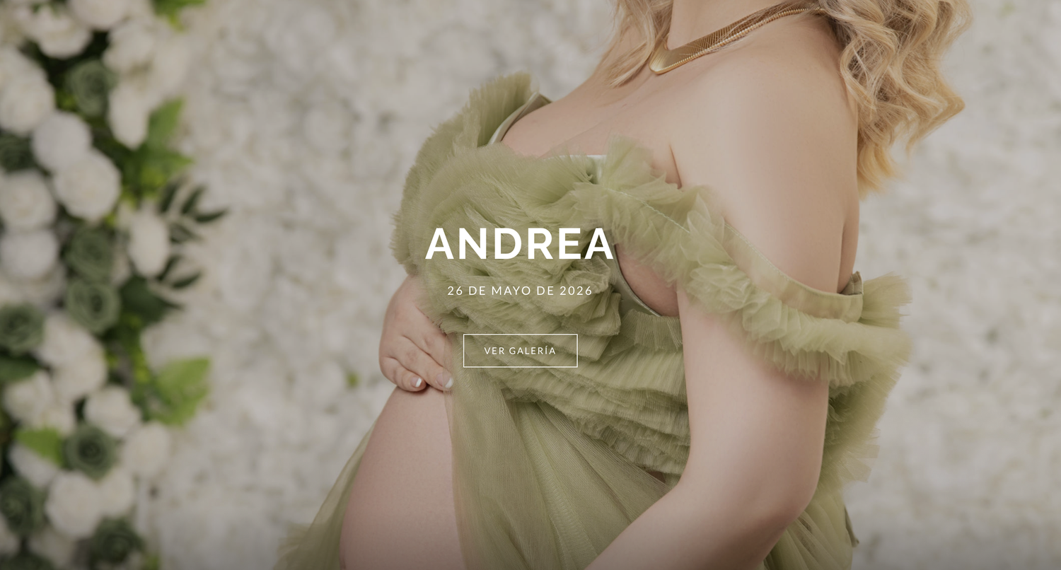Pregnant woman in elegant green tulle dress posing for maternity photoshoot with floral backdrop.