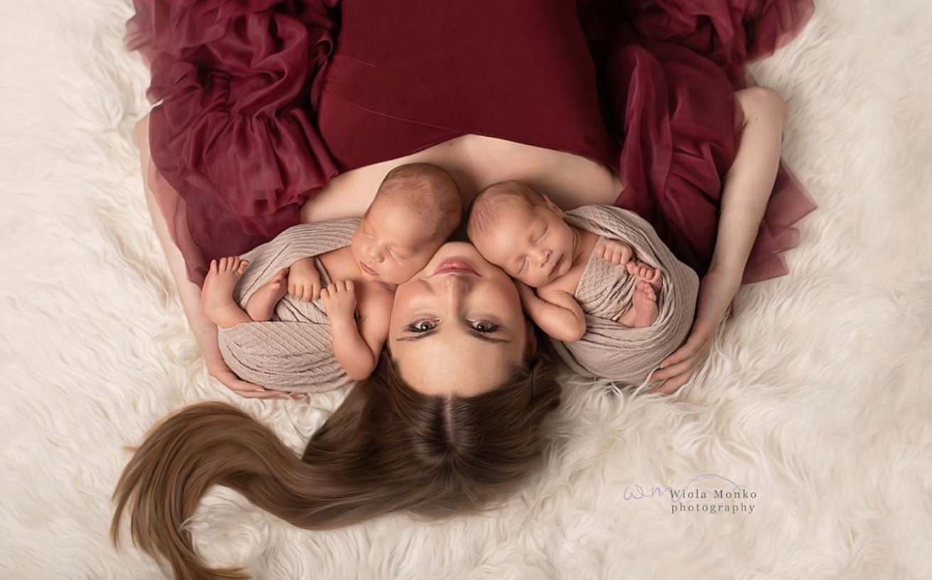 A woman in burgundy dress lies on white bedding in a dreamy boudoir photoshoot.