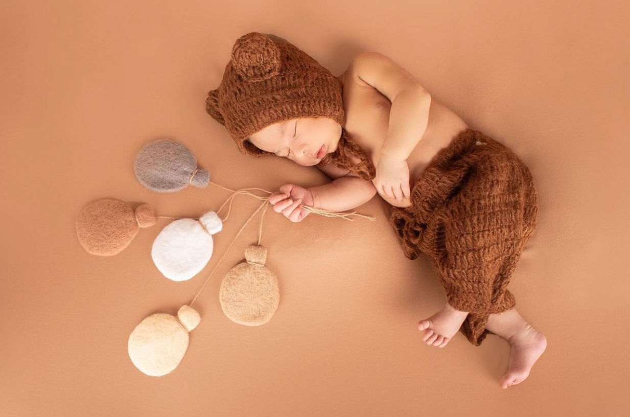 Newborn baby feet gently resting on warm peach-colored background in artistic photography series.