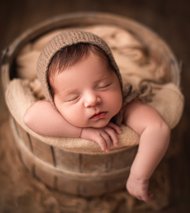 Sleeping newborn wrapped in beige blanket on neutral backdrop in professional studio photography.