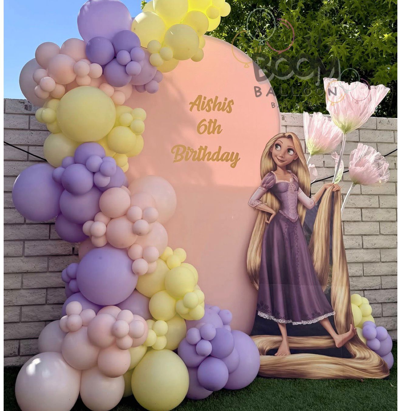 Rapunzel-themed 6th birthday party backdrop with pastel balloon garland arch in purple, yellow, and pink.