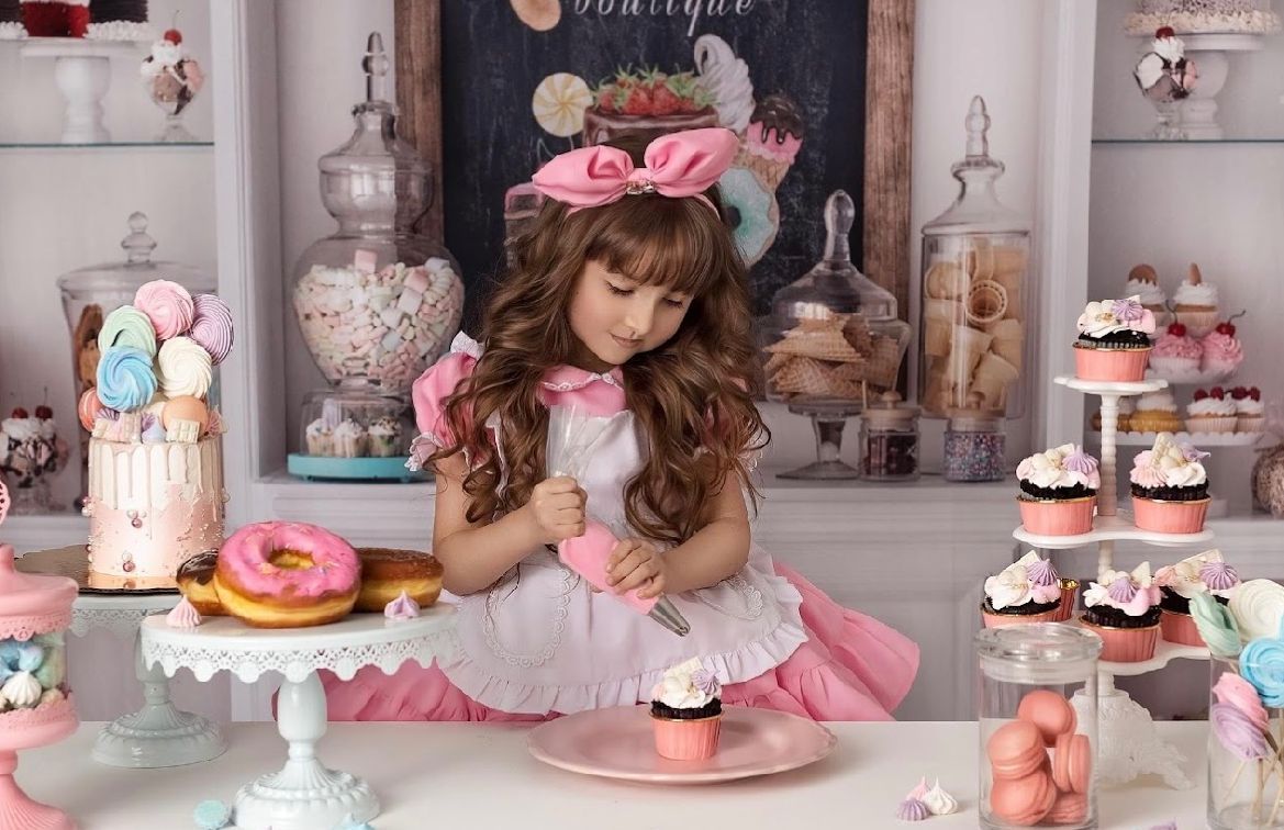 Sweet dessert display with pink and white decor featuring cupcakes, macarons, and glass candy jars in a pastel themed setting.