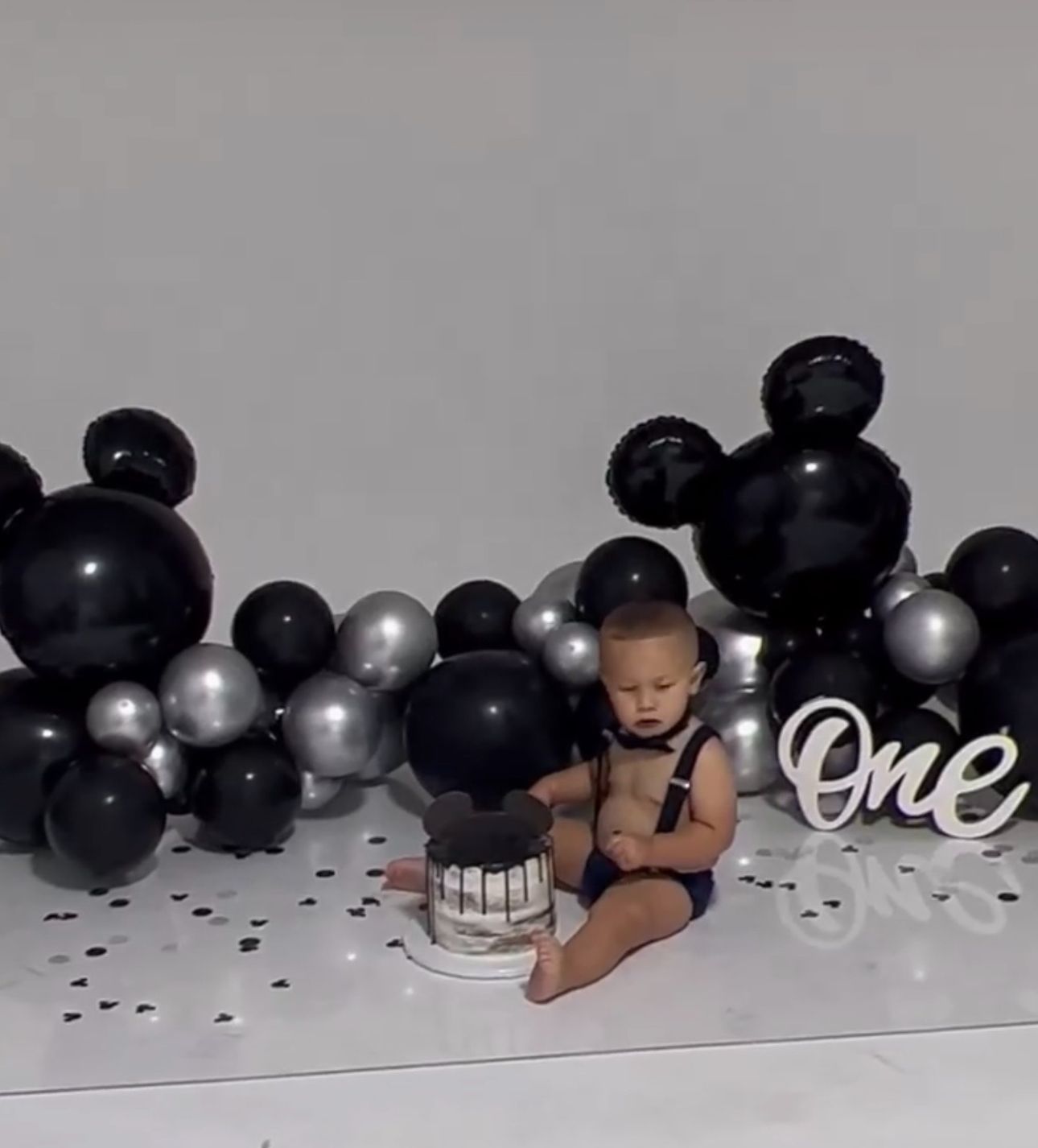 Black and silver balloon arrangement with scattered confetti on floor for birthday celebration.