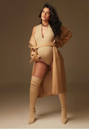 Fashion model poses in neutral beige monochromatic outfit against warm brown studio backdrop.
