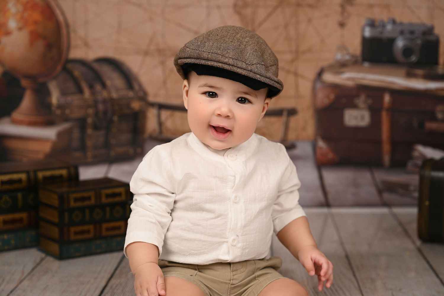 Baby wearing vintage style outfit with newsboy cap surrounded by antique props.