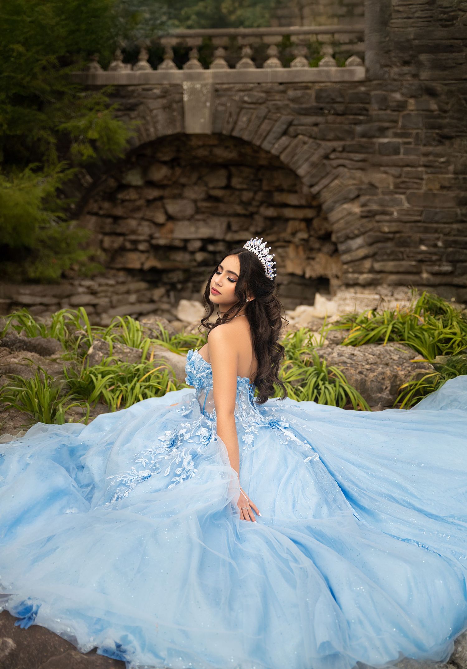 Fairytale portrait in flowing blue ball gown against stone castle architecture.