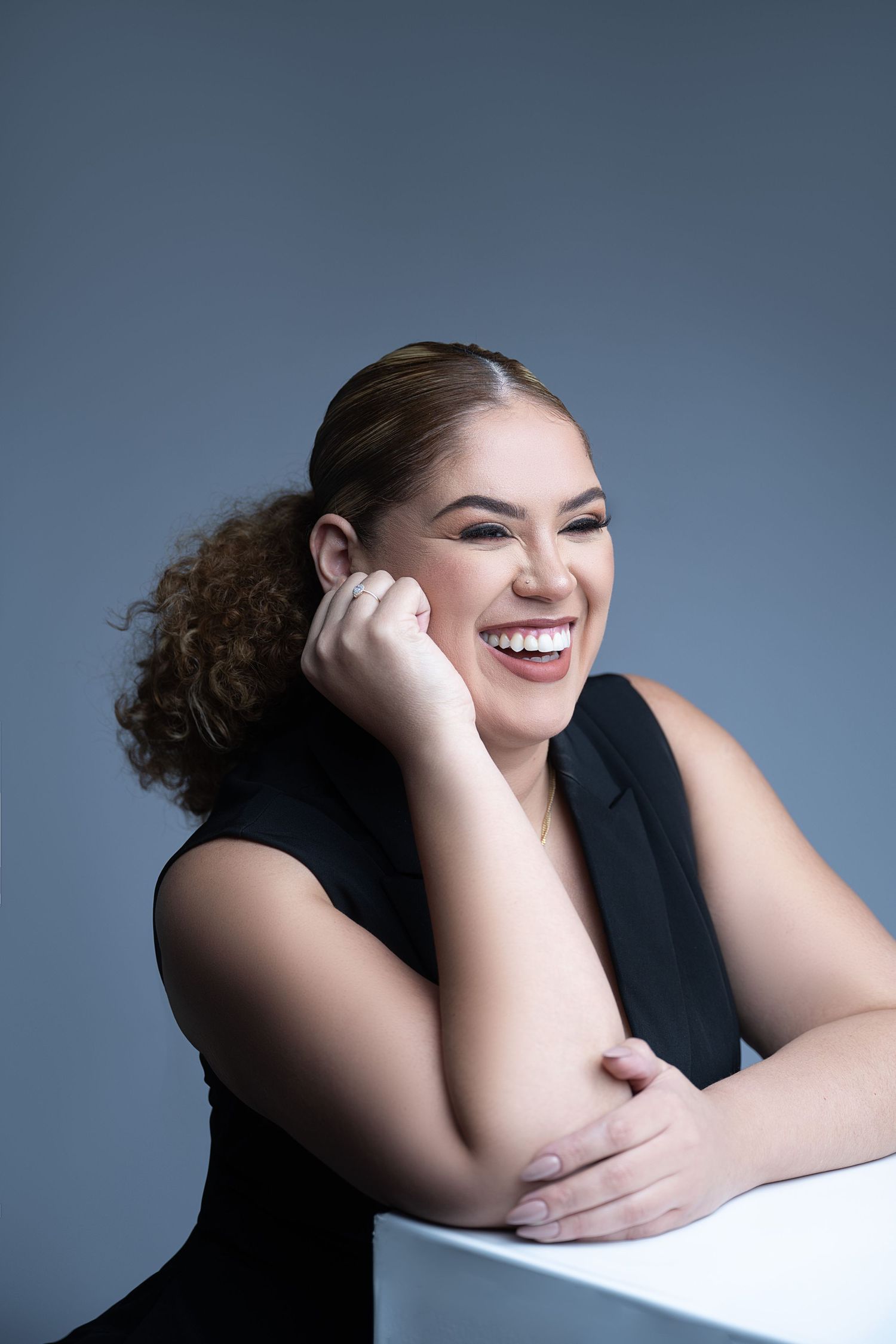 Studio portrait of someone laughing while leaning on a white surface against a blue background.