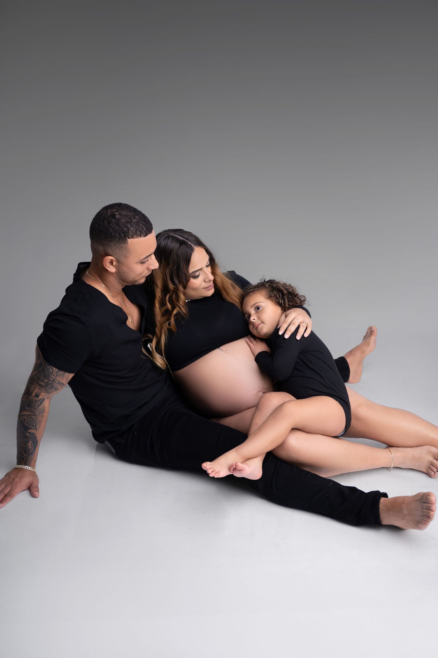 A series of black and white photos showing a couple in black clothing lying down in intimate poses against a light background.