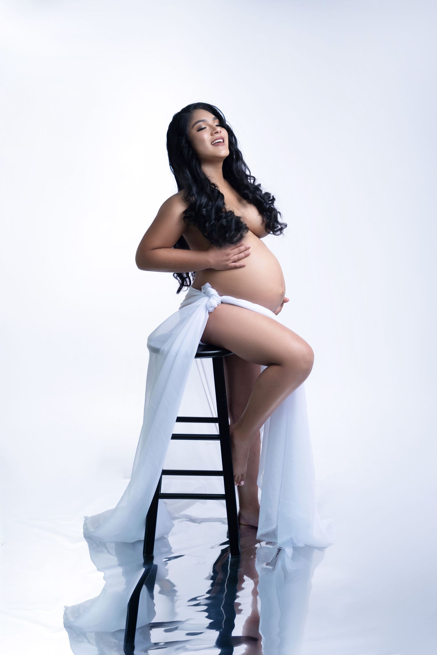 Artistic maternity boudoir photo with flowing white fabric against white background.