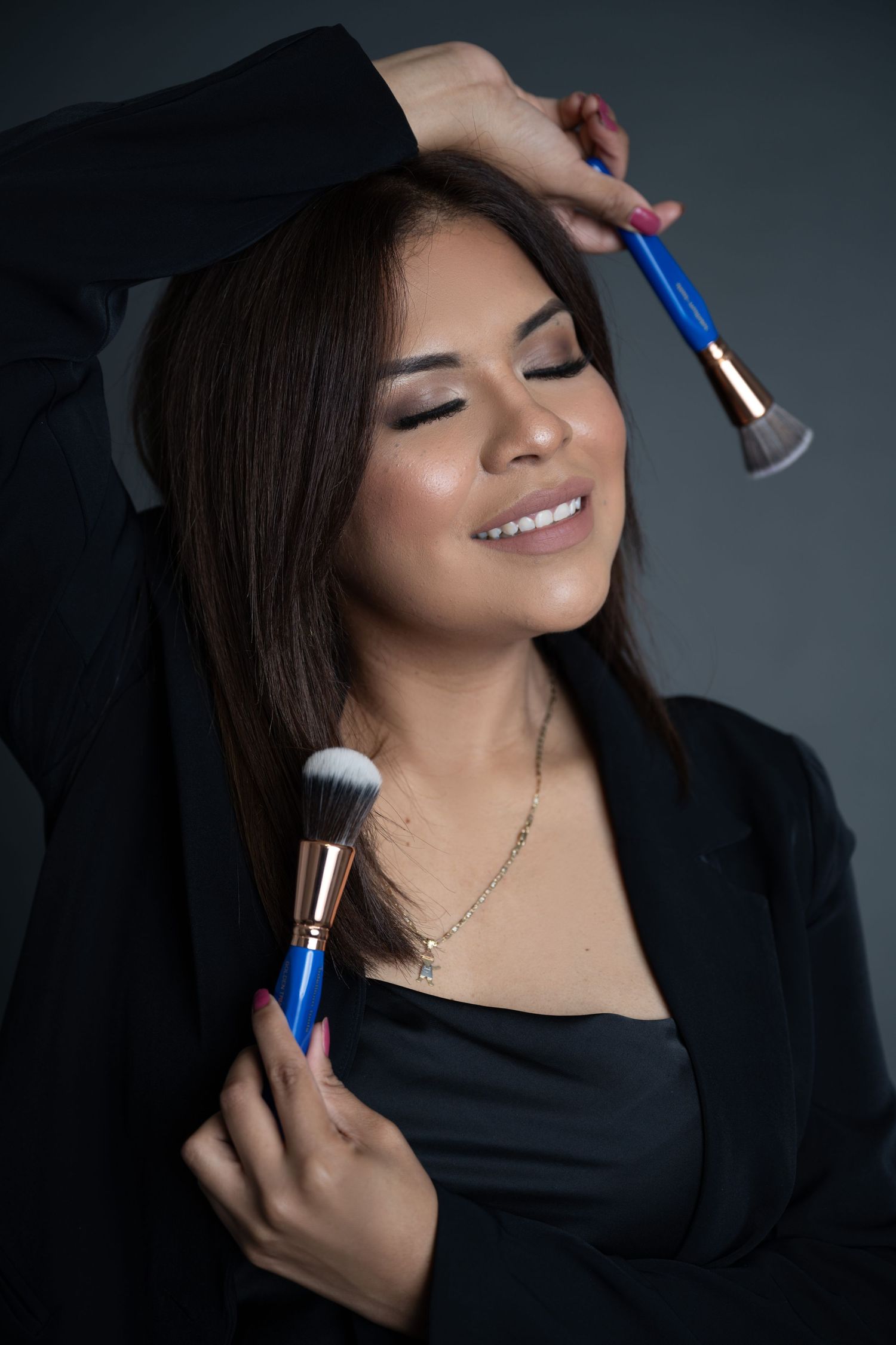 Beauty artist holding makeup brushes with closed eyes and serene expression.