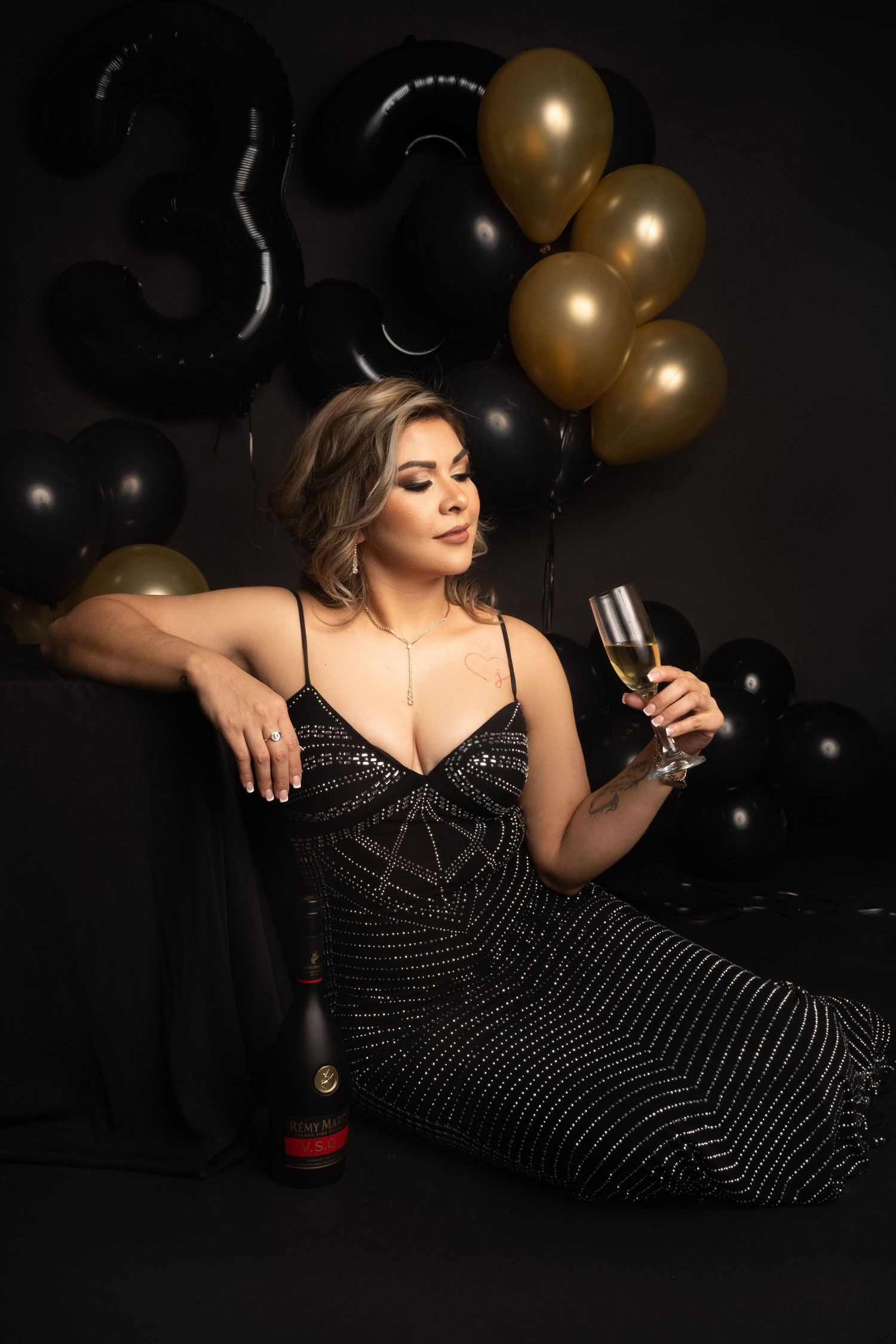Glamorous party scene with sparkly dress, champagne, and black and gold balloon decorations.