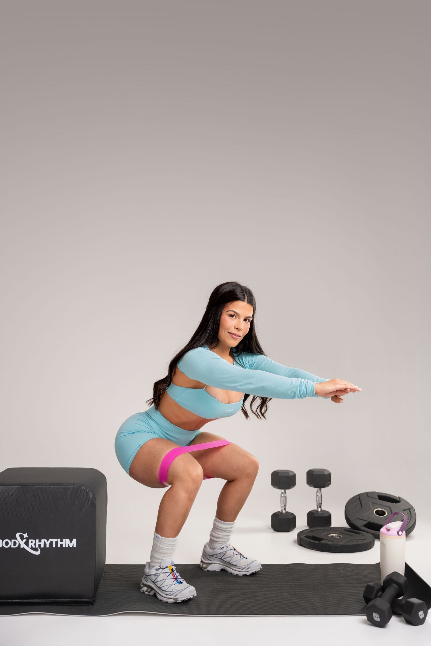 Woman in blue activewear doing squats with resistance band, dumbbells and Body Rhythm equipment nearby.