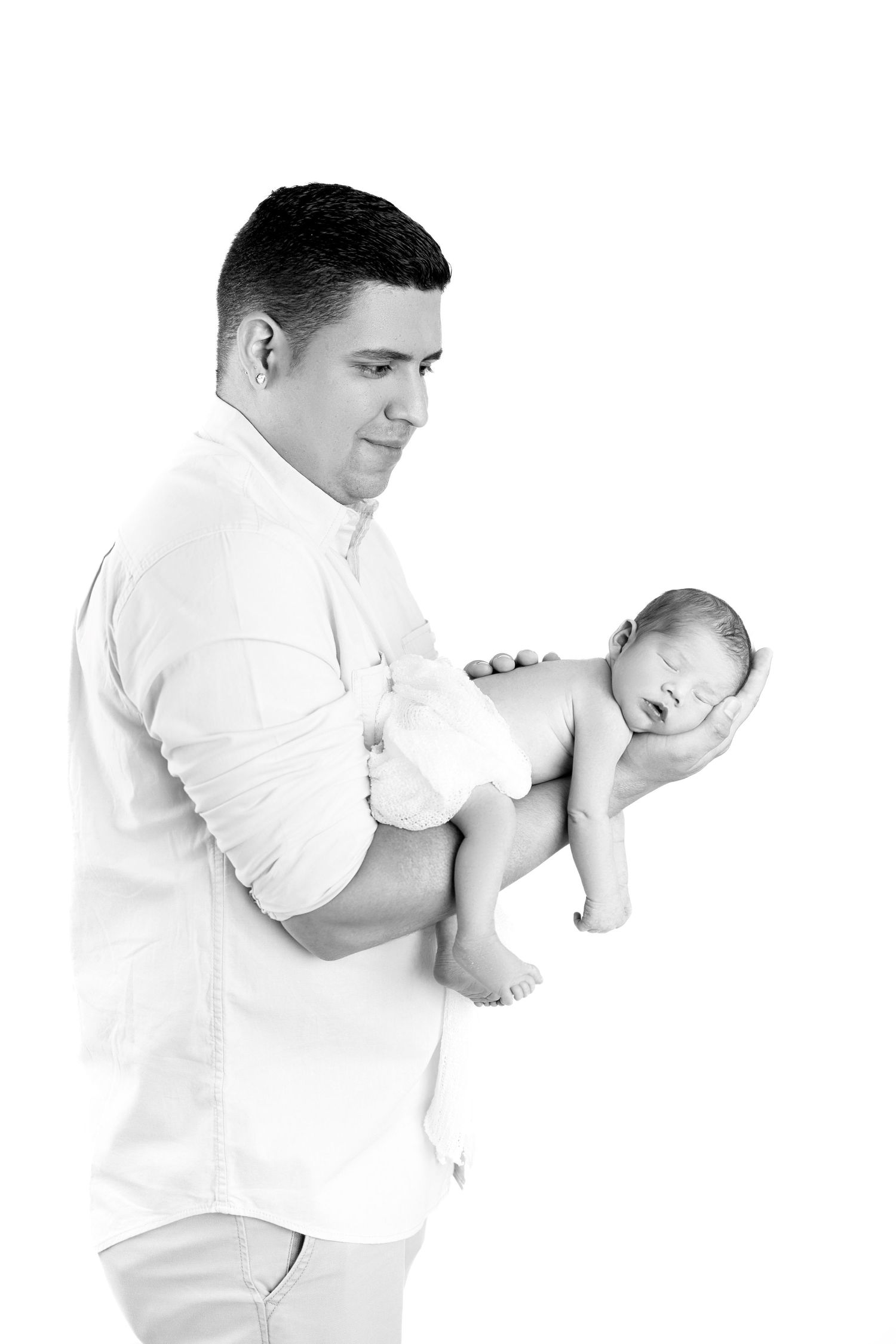 Black and white photo of a father tenderly holding his sleeping newborn baby against a white background.