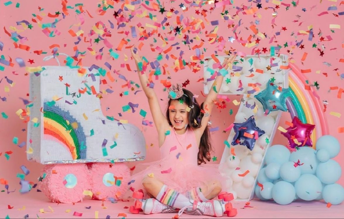 Colorful confetti explosion against pink background with unicorn decorations and rainbow elements.