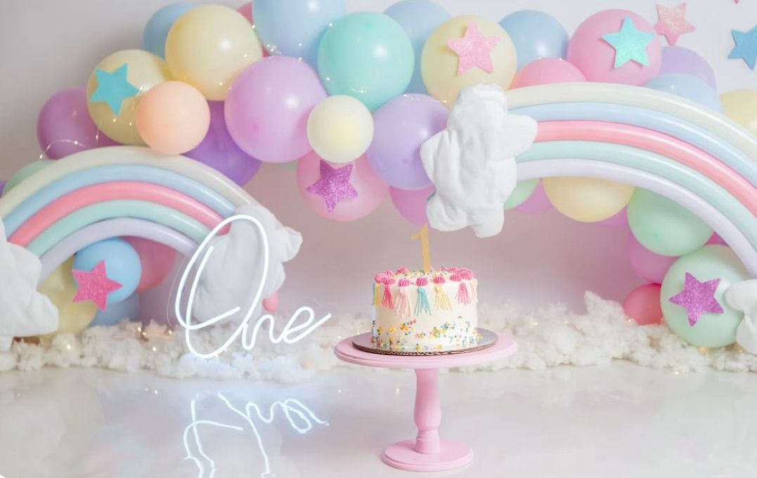 Pastel rainbow balloon arch with clouds and stars decorates a dreamy party setup with pink and blue accents.