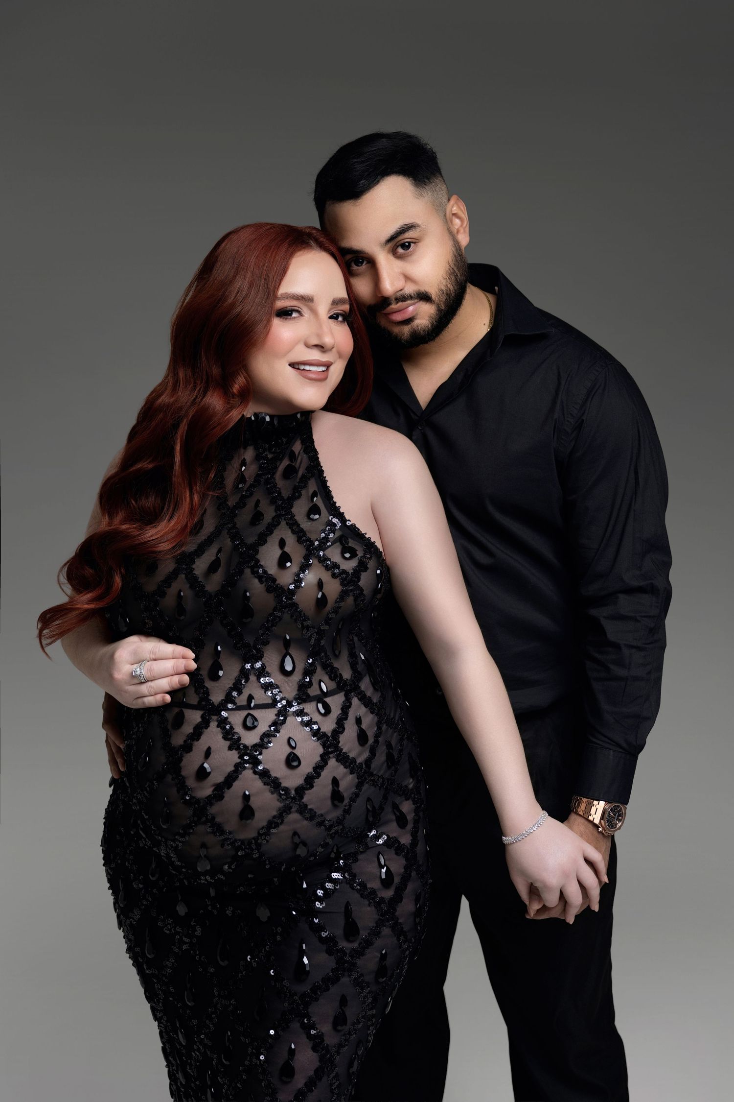 A romantic couple poses together against a gray backdrop in a series of intimate black and white portraits.