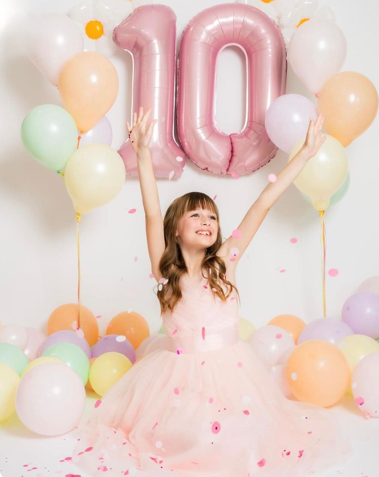 A joyful girl in a pink tulle dress celebrates her 10th birthday with colorful balloons and confetti.