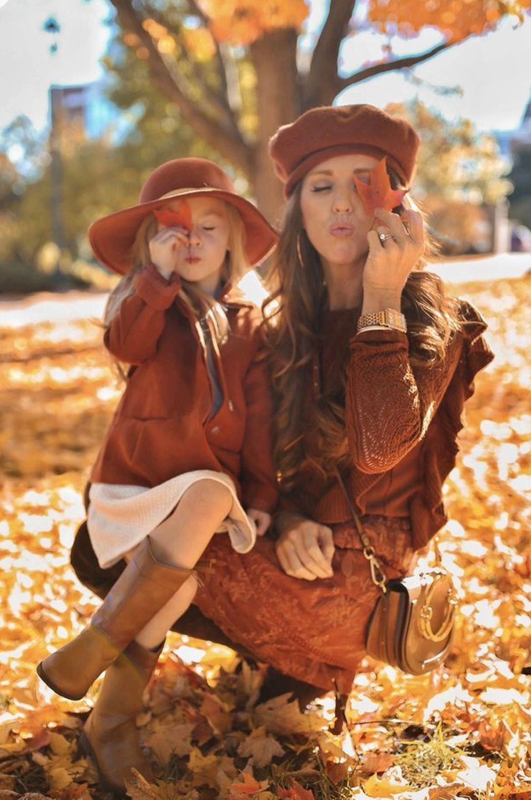 A person wearing a brown vintage dress and hat lies in autumn leaves while reading a book on a fall day.